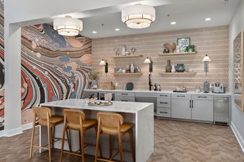 A kitchen with a large mural on the wall and a marble island with three chairs.